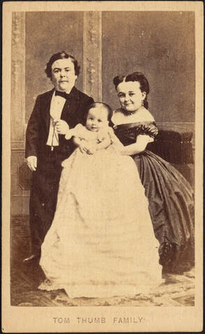 A sepia tone family portrait of dime museum performers  Tom Thumb and Lavinia Warren. Tom Thumb is on the left in a black suit, white shirt, and black bowtie. Lavinia is smiling on the right in a black dress. In between them is a baby dressed in a long white gown. Below the portrait, the words 